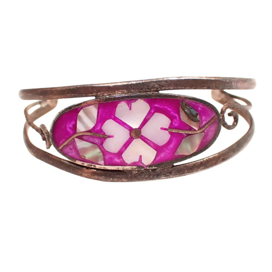 Front view of the Alpaca fuchsia flower cuff bracelet. The silver tone metal has darkened from age to a dark gray color. There is an oval area on the front with pink purple enamel that has inlaid mother of pearl and abalone shell forming a flower design.