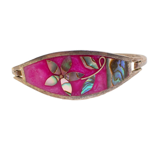 Front view of the Alpaca vintage hinged bangle bracelet. The metal is darkened to an antiqued silver color from age. The front is wider in the middle. About two thirds of the front on the left side has pearly fuchsia color enamel. There is a flower with marquis shaped petals and leaves and the other about third area on the right that are made up of iridescent pieces of abalone shell.