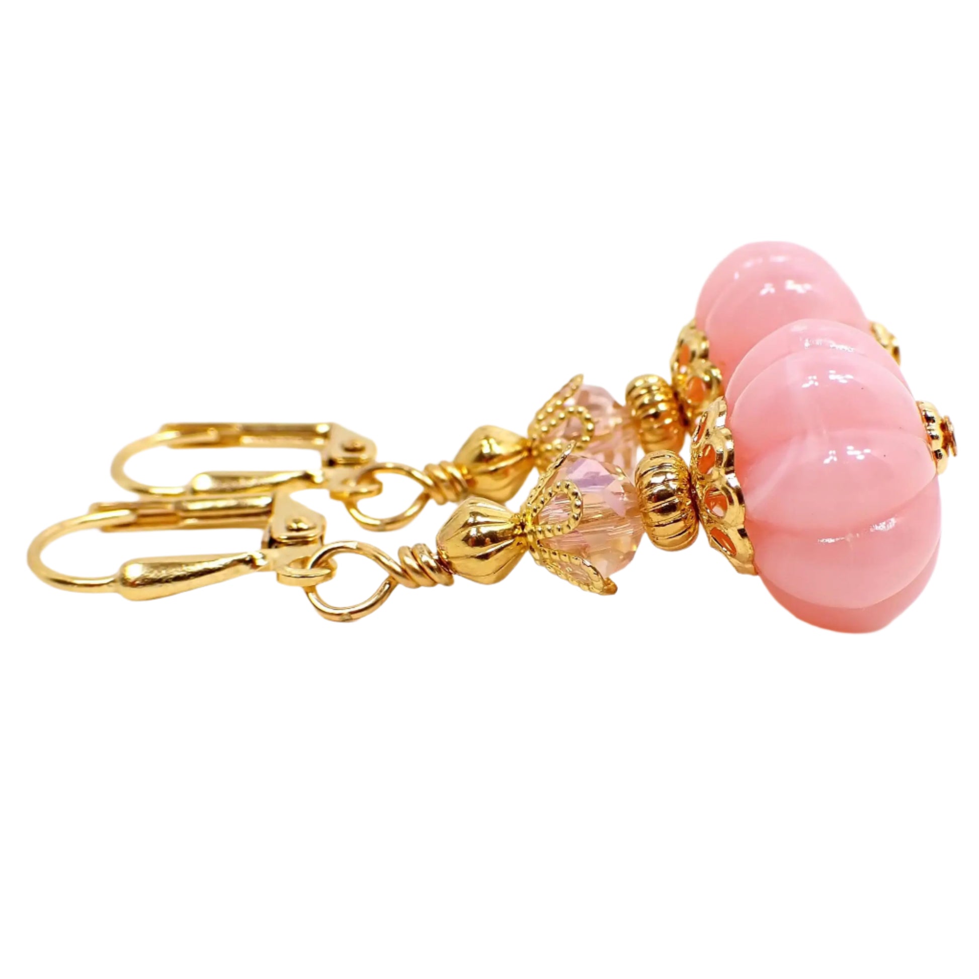 Side view of the handmade drop earrings with vintage lucite beads. The metal is gold plated in color. There is a new faceted glass crystal bead at the top in light pink. The bottom bead is pumpkin shaped and is light pink lucite with gentle swirls of white here and there.