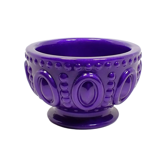 Angled side view of the handmade resin footed bowl. It's round with an oval and dot pattern around the outside of it. The resin is a vivid pearly purple in color.