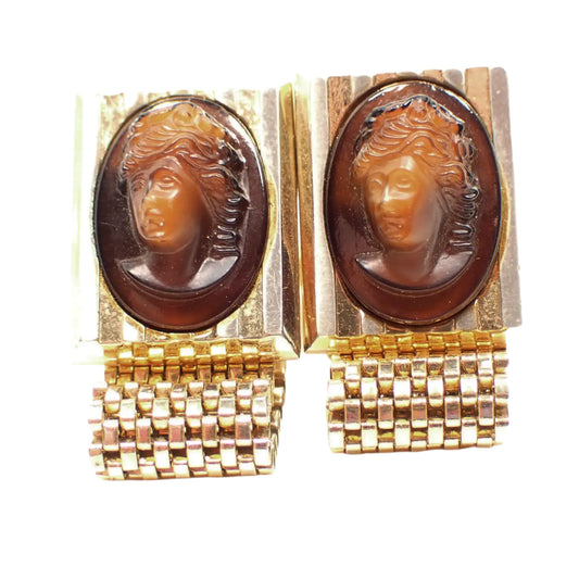 Front view of the Mid Century vintage Hickok cameo cufflinks. The metal is gold tone in color. The top part has a faceted rectangle area with a glass oval cameo in the middle. The cameos have different shades of brown and have a woman's head facing to the left.