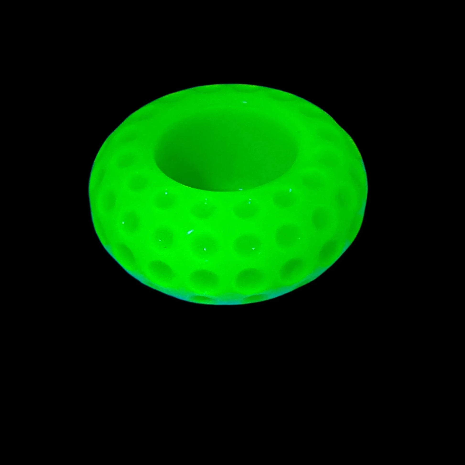 Photo showing how the handmade neon yellow resin candle holder fluoresces under a UV light in a bright yellow green color. The candle holder is round saucer shaped with indented dots all the way around it. There is an area on the top for the candle.   