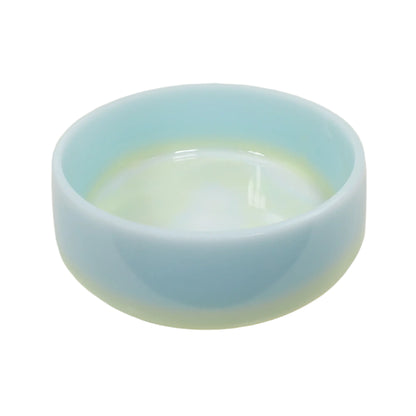 Angled side view of the large handmade pastel blue, yellow, and white resin decorative bowl. It is round with a slightly flared out bottom. The bowl is mostly light blue in color with a band of yellow and marbled white on the bottom.