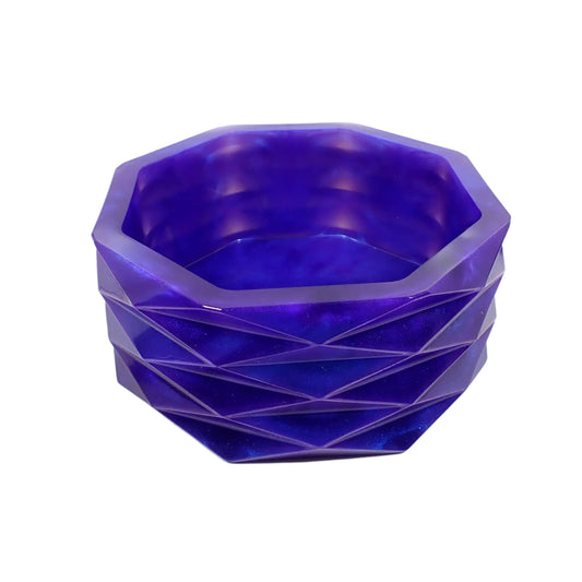 Angled side view of the handmade iridescent purple geometric bowl. It has an overall octagon shape with faceted diamond shapes on the side all the way around it. The resin is shiny and pearly in an iridescent purple color that has highlights of blue as the light hits it. Great for use as a succulent planter pot, as part of your table centerpiece, or just to add a pop of color to your home decor.