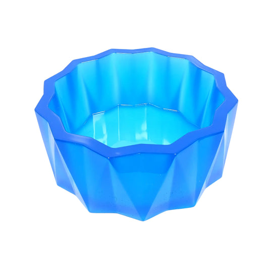 Angled side view of the large handmade neon blue resin faceted decorative bowl. It has a sun like faceted shape on top and a faceted triangle design on the sides with the triangles alternating in direction. The resin is shiny and semi translucent in a neon ocean blue color. 