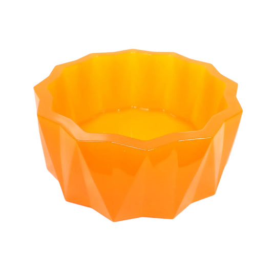 Angled side view of the large handmade neon orange resin faceted decorative bowl. It has a sun like faceted shape on top and a faceted triangle design on the sides with the triangles alternating in direction. The resin is shiny and semi translucent in a bright neon orange color. 