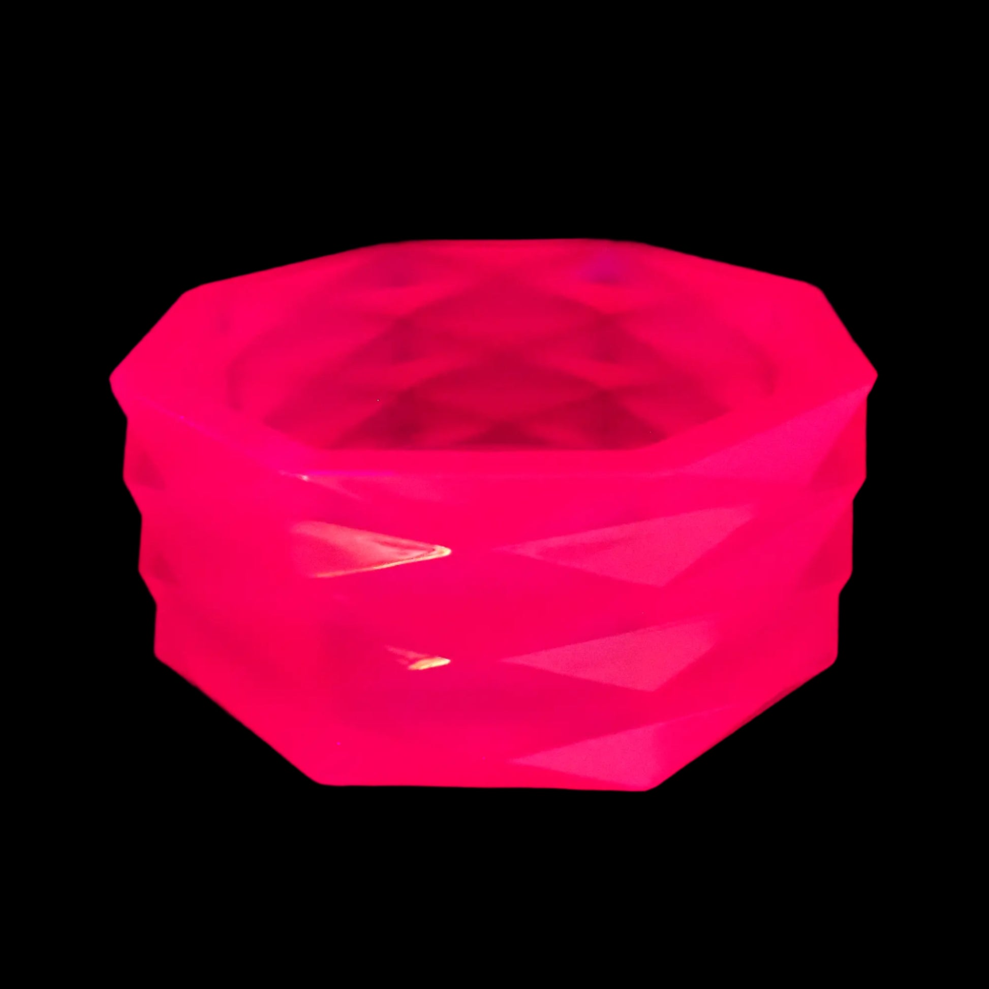 Image of the large handmade neon pink resin geometric bowl under a UV light showing that it is fluorescent and glows pink in color. 