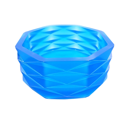 Angled side view of the large handmade neon blue resin decorative bowl. It has an overall octagon shape with a faceted diamond shape design all the way around the outside. The resin is shiny and semi translucent in an ocean neon blue color.