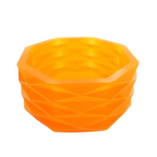 Angled side view of the large handmade neon orange resin decorative bowl. It has an overall octagon shape with a faceted diamond shape design all the way around the outside. The resin is shiny and semi translucent in a citrus neon orange color.