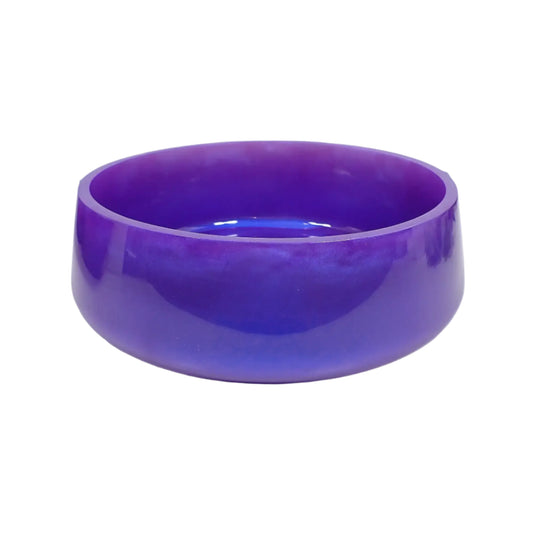 Angled side view of the handmade resin decorative bowl. It has a large round shape with a slightly flared bottom. The resin is shiny and opaque in a pearly iridescent purple color that has flashes of blue as the light hits it. Great piece to use as part of your table centerpiece home decor.