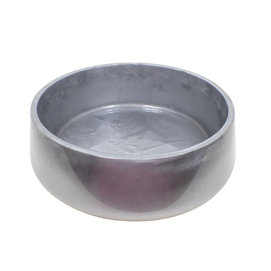 Angled side view of the large metallic silver resin decorative bowl. It is round with a slightly flared bottom. The resin is shiny and opaque with swirls of different shades of metallic silver colors. 