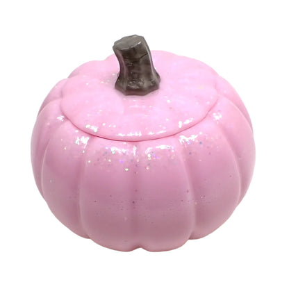 Angled view of the handmade resin pumpkin trinket box. It has light opaque shiny pink resin with pastel iridescent glitter on the top part of the pumpkin. The stem is a pearly light brown color.