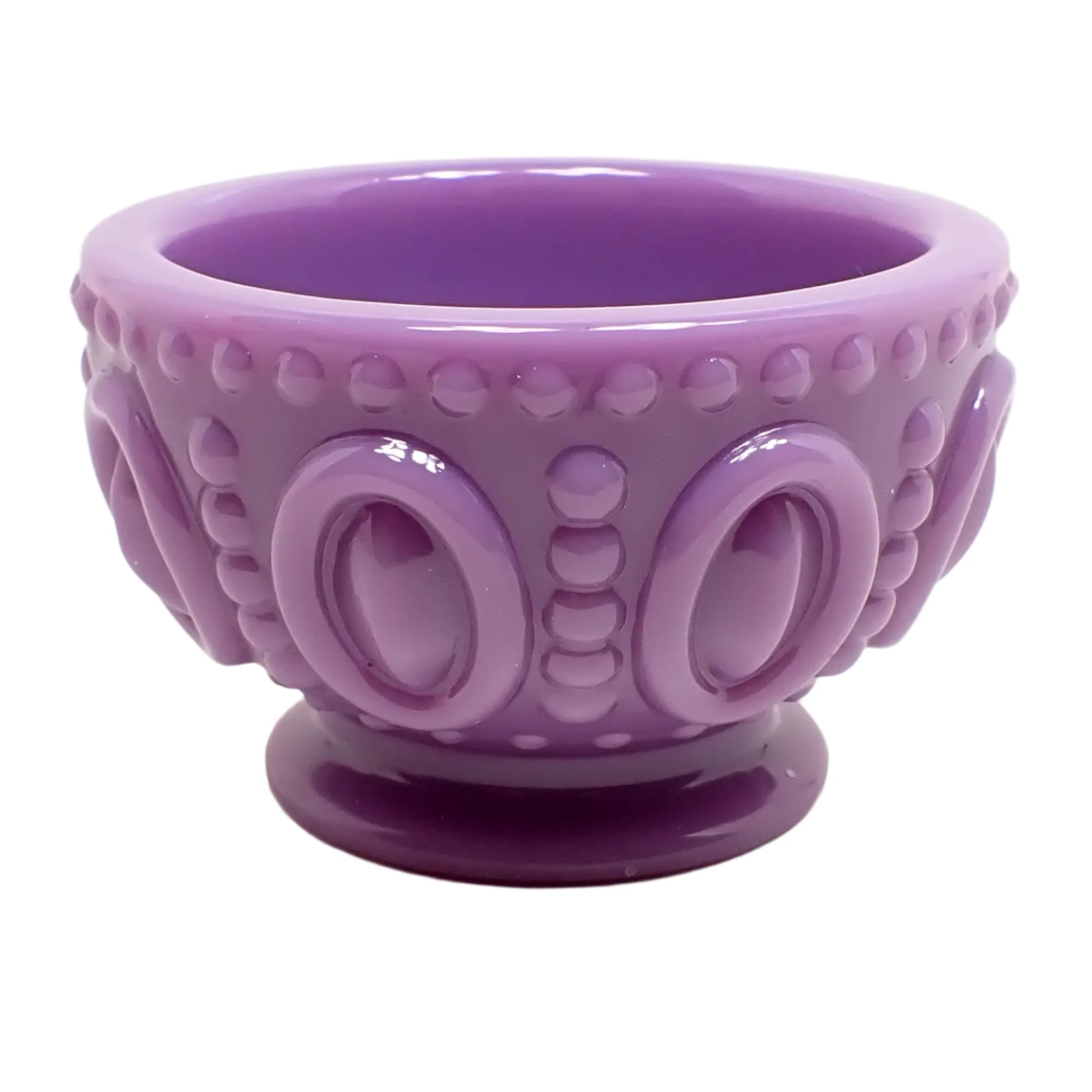 Angled side view of the light purple resin footed bowl. It is round with a pastel lavender colored resin. There are large ovals around the outside with a line of dots in between them and around the top and bottom edge. 