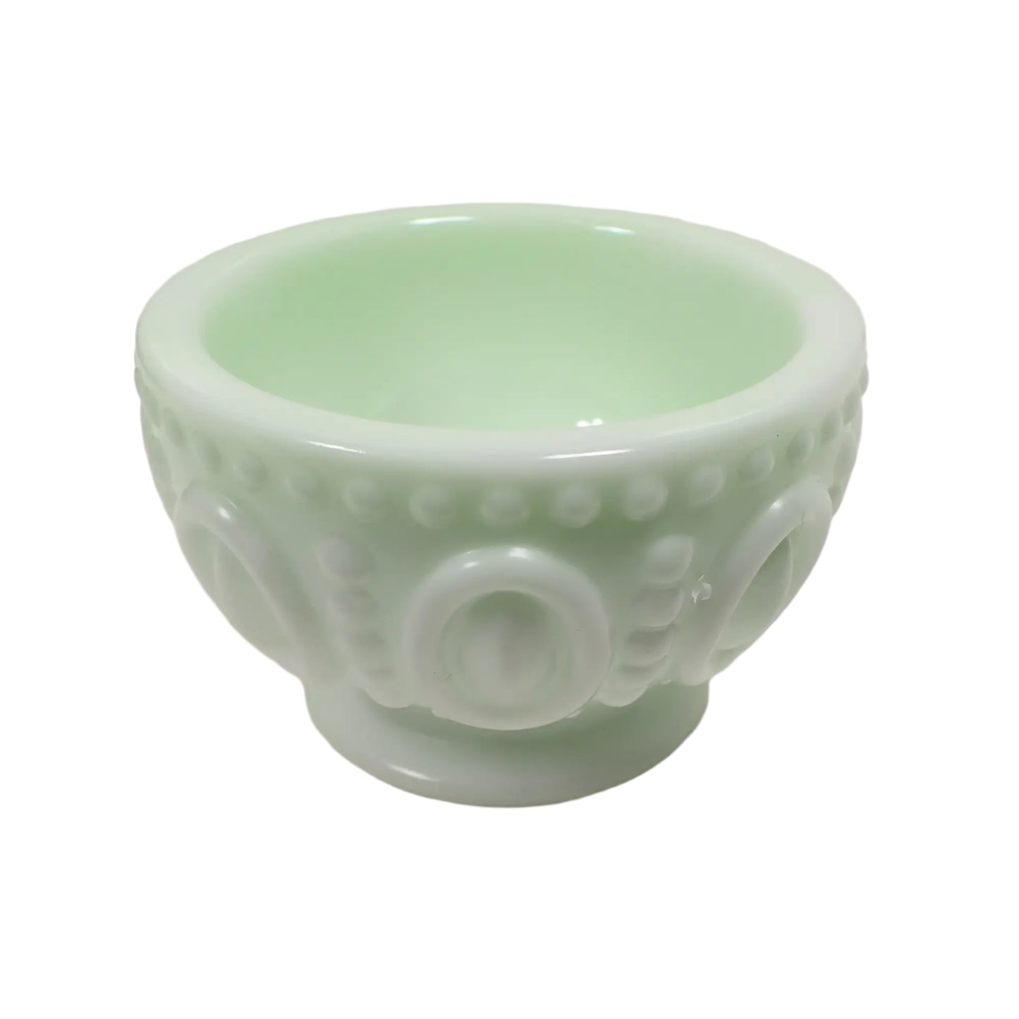 Angled side view of the handmade resin footed bowl. It is round with a raised dot and oval pattern around the outside. The color is a very light pastel green with hints of white marbled in.