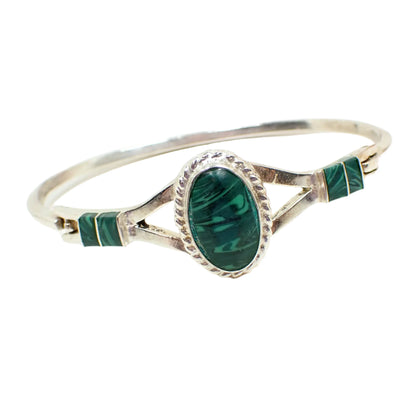 Angled view of the vintage malachite gemstone hinged bangle bracelet. Here the swirls and stripes of light and dark green on the malachite can be seen clearly.