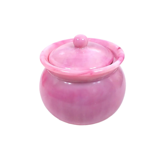 Angled side view of the handmade resin decorative jar. It is round with a raised edge that flares outward. The round lid fits inside that area and has a small round knob used to lift the lid off. The resin is opaque and shiny and has marbled shades of pastel pink. Great for storing small items or just for adding to your home decor. 