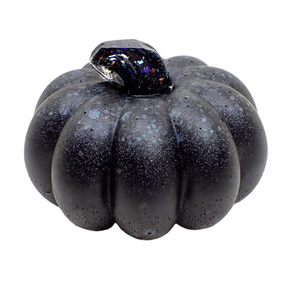 Side view of the handmade resin pumpkin. It has matte black resin on the pumpkin with glitter that shows softly through as colorful speckles. The stem is shiny and the glitter shows as sparkles of different colors.