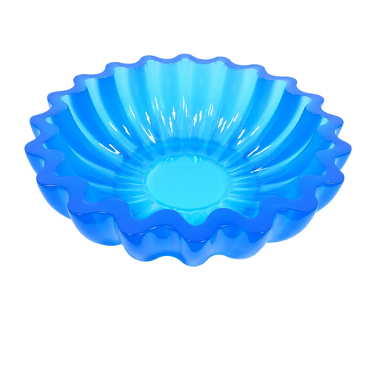 Angled side view of the handmade neon blue resin scalloped decorative bowl. It is round with fluted sides and a scalloped top edge. The bottom is tapered. The resin is shiny and semi translucent in an ocean neon blue color. 