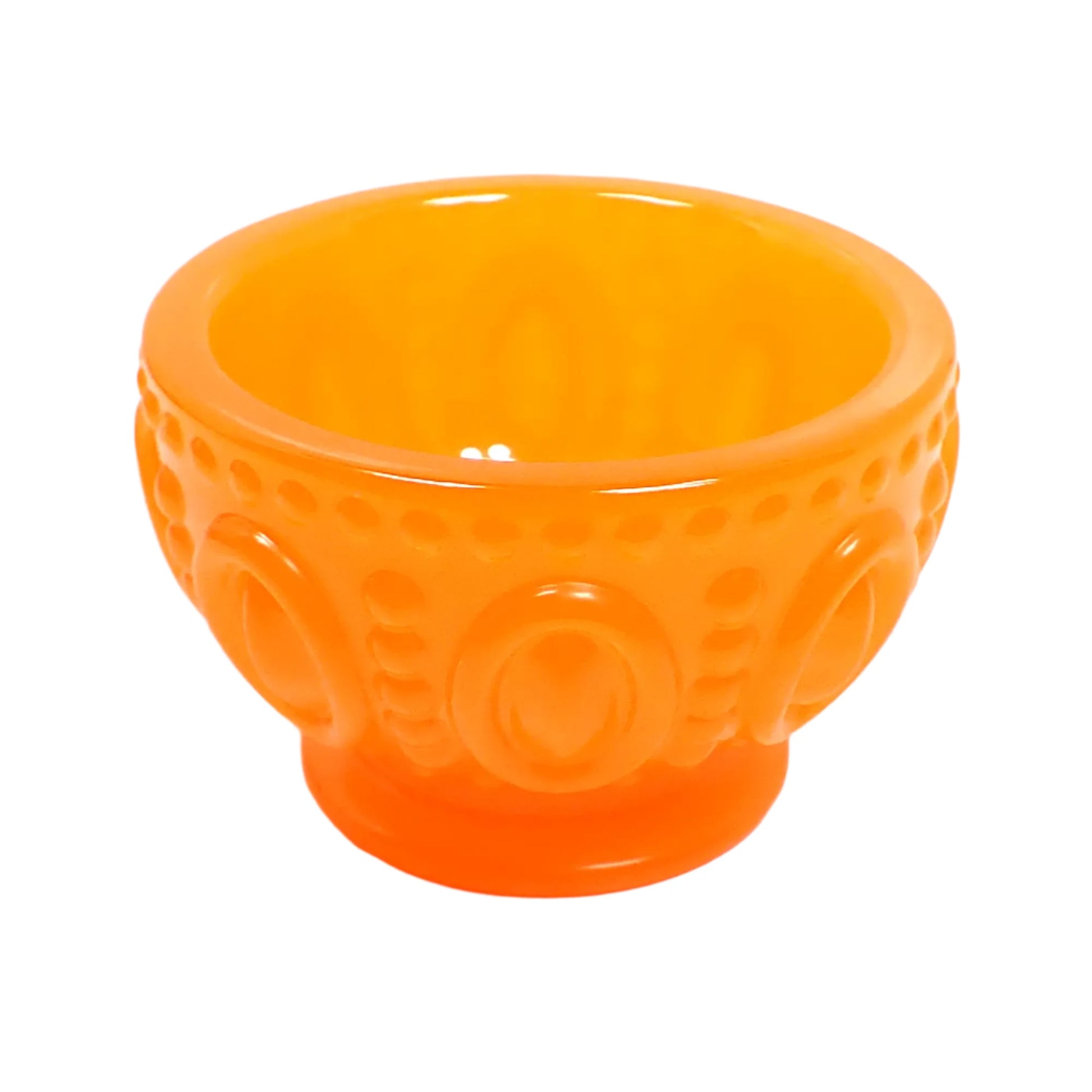 Angled side view of the handmade resin footed bowl. It is round with an oval and dot design all the way around it. It is neon orange in color.