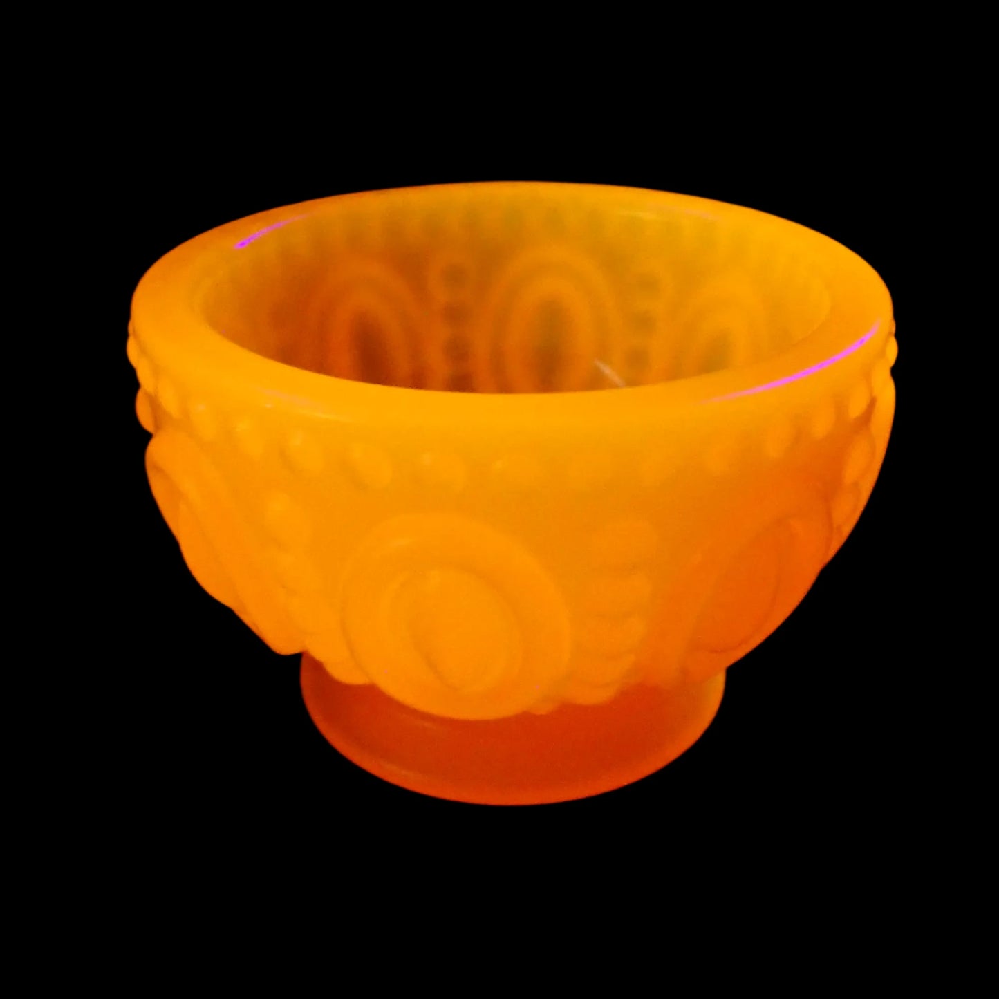 Photo of the handmade neon orange resin footed bowl under a UV light showing how it fluoresces a bright orange.