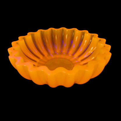 Image of the handmade neon orange resin scalloped bowl showing that it is fluorescent. It is glowing a bright orange color under a UV light.
