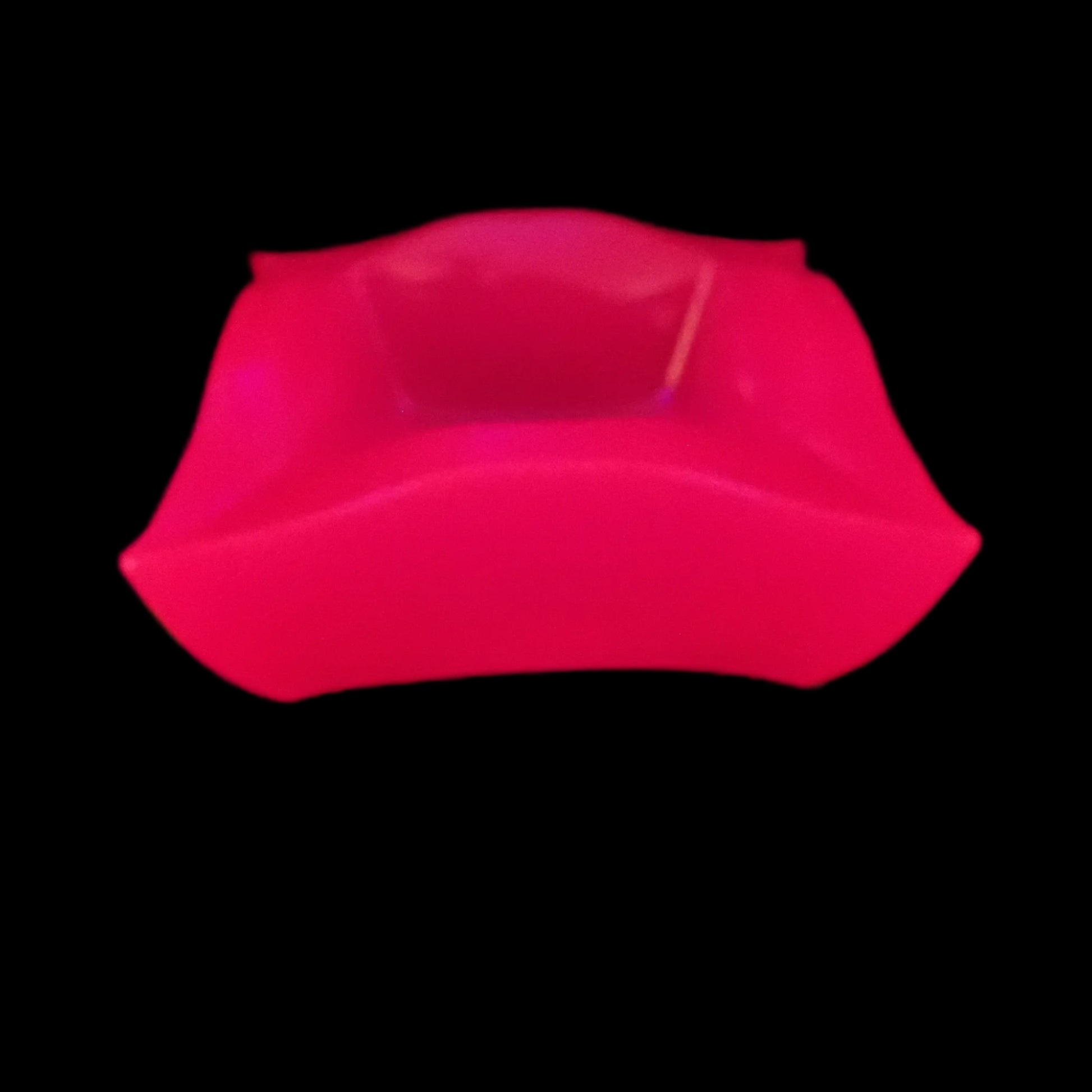 Image of the large handmade neon pink resin retro atomic style decorative bowl under a UV light showing that it is fluorescent and glowing a bright pink in color.