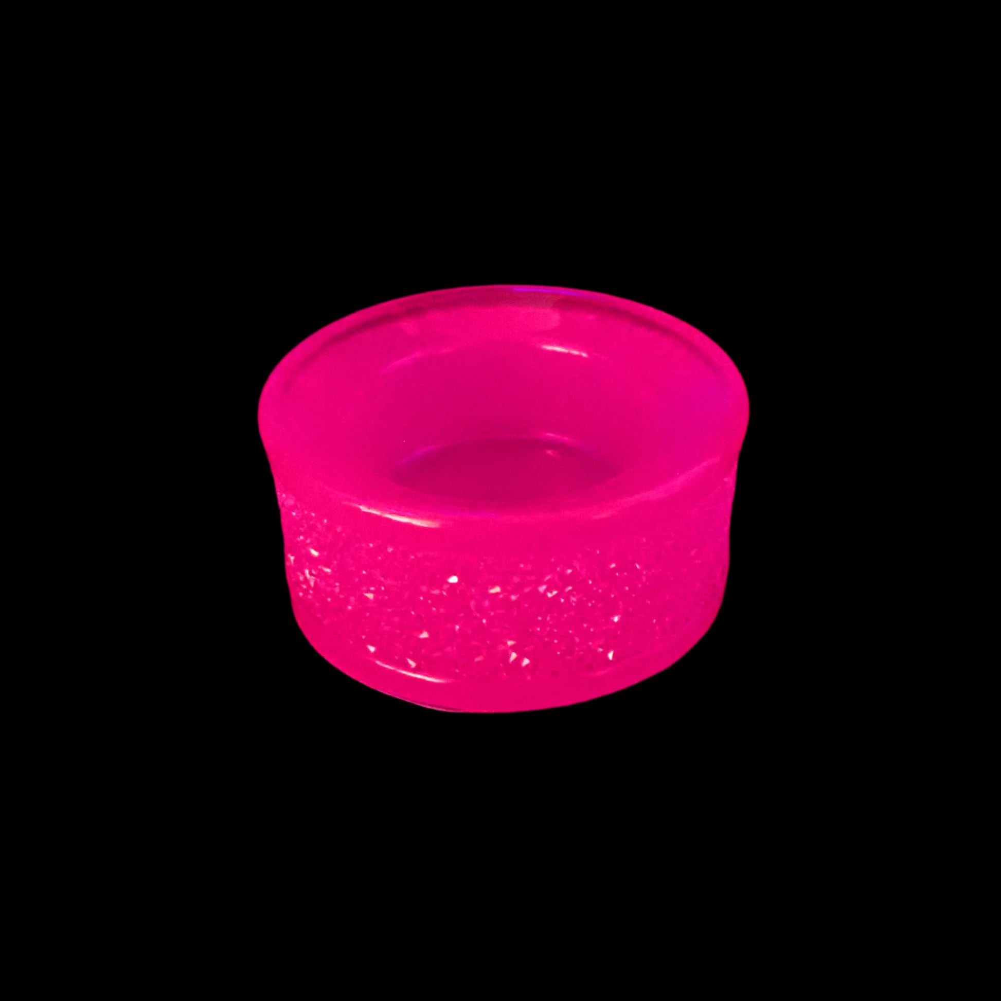 Image of the handmade neon pink resin tealight candle holder under a UV light to show how it glows a bright pink in color.
