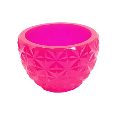 Angled side view of the handmade resin bowl. It is bright neon pink and has a round design with a tapered bottom. There is a retro style faceted design around the outside of the piece. 