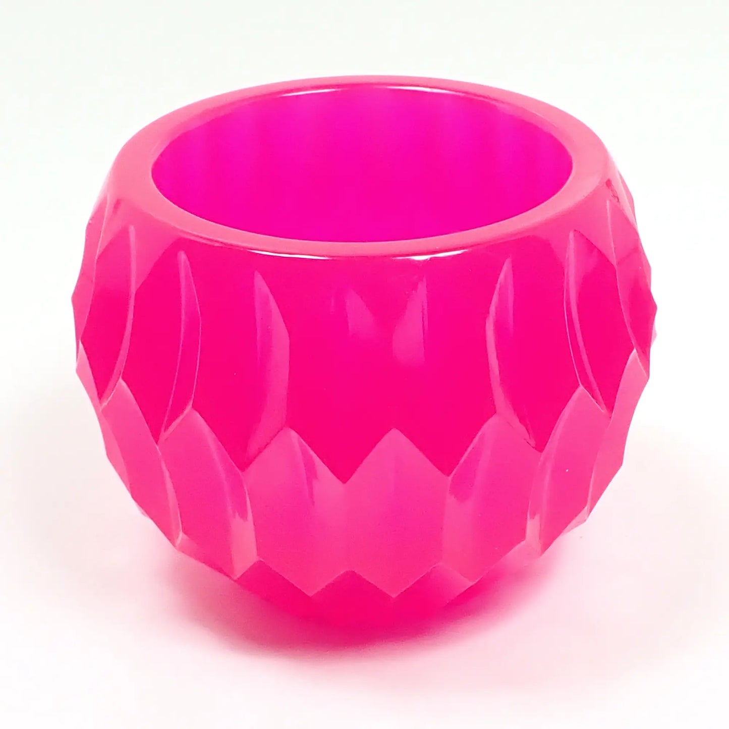 Angled side view of the handmade resin succulent pot decorative bowl. It is bright neon pink in color and is round with an indented hexagon shape design.