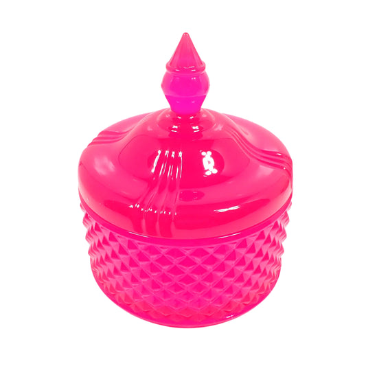 Angled top view of the handmade neon pink resin trinket box showing more of the top. The top is shiny and smooth with a tapered knob in the center to lift the lid with. The bottom is round and has a raised diamond shaped pattern design all the way around it. The resin is semi translucent and a bright neon pink color. Great for adding a pop of color to your fluorescent home decor. 