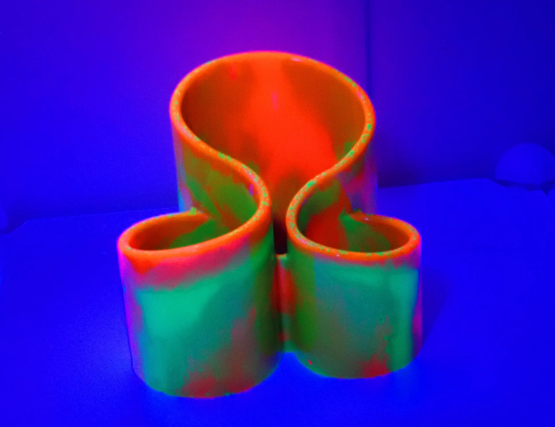 Photo showing how the neon makeup brush holder fluoresces under a UV light. The orange and green colors have a bright glow to them.