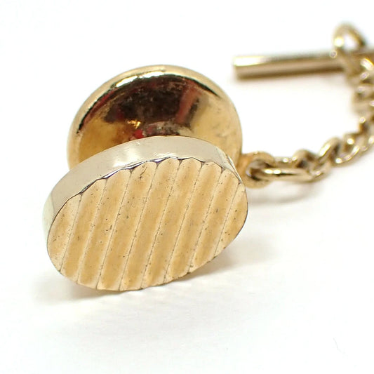 Front view of the retro vintage tie tack. The metal is gold tone in color. It is oval in shape with diagonal diamond cut etched lines on it.