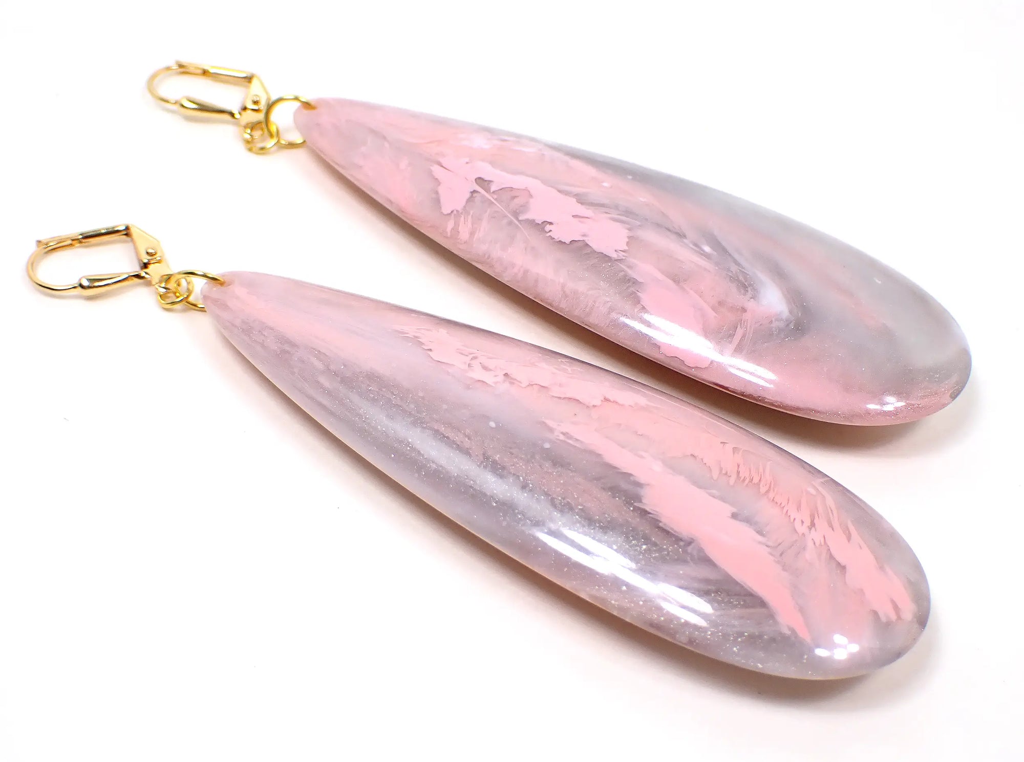 Angled view of the handmade large teardrop earrings. The metal is gold plated in color. There are very large long acrylic teardrops that have marbled pink and gray colors.