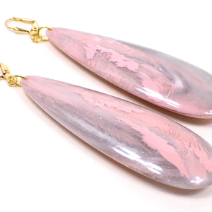 Angled view of the handmade large teardrop earrings. The metal is gold plated in color. There are very large long acrylic teardrops that have marbled pink and gray colors.