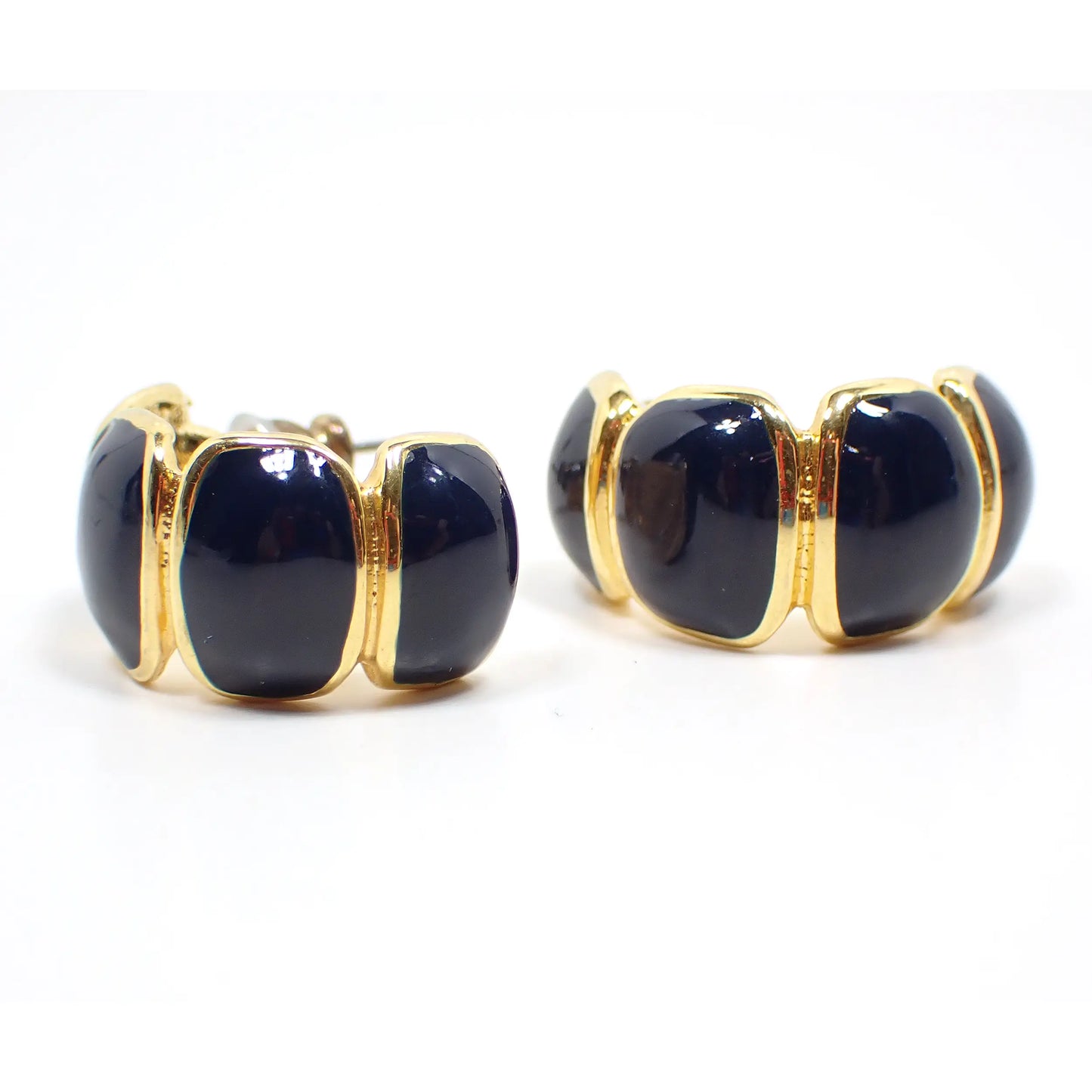 Front view of the retro vintage enameled half hoop earrings. They are U shaped and have gold tone plated metal. There are irregular oval like shapes with dark blue enamel inside each. You can see the post back on one of the earrings from this angle.