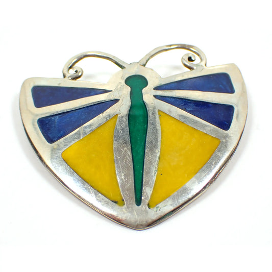 Front view of the retro vintage Alpaca Mexico butterfly brooch pendant. The metal is silver tone in color. Brooch is shaped like a butterfly with blue and yellow enameled wings and a green enameled body. A few small spots of verdigris can be seen on the antenna area under magnification.