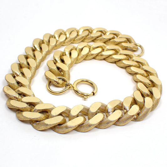 Top view of the retro vintage wide Cuban link curb chain necklace. The metal  is gold tone plated in color. There are wide curb links with textured sides and flat cut edges on the top and bottom. There is a large spring ring clasp at the end.