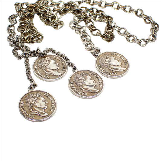 Enlarged view of the retro vintage faux coin medallion lariat necklace. The metal is mostly silver tone plated in color, but there is some darkened patina on the chain and faux coins from age. The chain is cable link with double rings and each link has one ring that is textured. This photo is showing the front view of the medallions with a depiction of Napoleon and the words Napoleon Empereur around the sides.