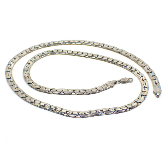 Top view of the retro vintage virola link chain. The sterling silver has a lightly darkened patina for a darker silver color. There is a lobster claw clasp at the end. The links are rounded flat and shaped like rounded V's that are hooked together. It is a wider chain. 925 marking can be seen on the link by the clasp.