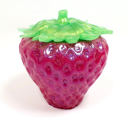 Side view of the handmade resin strawberry trinket box. The lid is pearly green in color. The bottom is bright pearly pink with iridescent pink glitter.