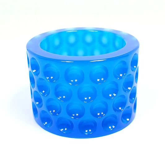 Side view of the decorative handmade resin trinket dish. It has a round cylindrical shape with an indented dot pattern all the way around it. The resin is a semi translucent neon blue color.