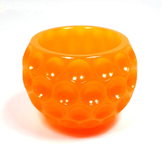 Side view of the handmade resin decorative bowl. The resin is bright orange in color. The bowl is rounded and has an indented dot design all the way around it.