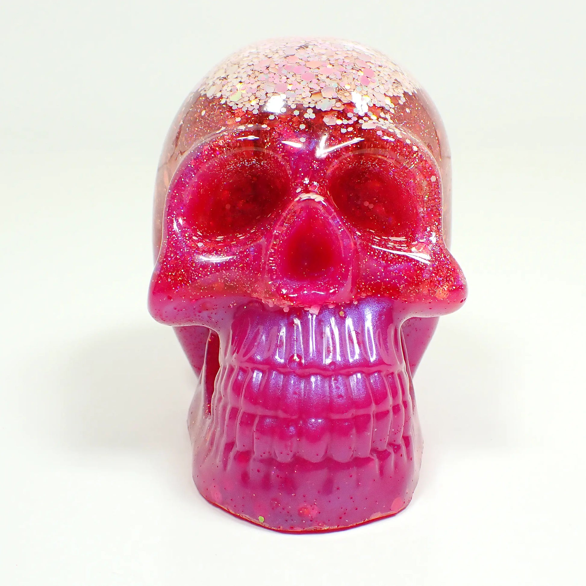 Front view of the handmade resin skull. There are two choices and this photo shows the one that has light pink iridescent glitter at the top followed by bright pink resin and iridescent glitter in the middle, and finally pearly bright pink resin at the bottom with some hints of glitter.