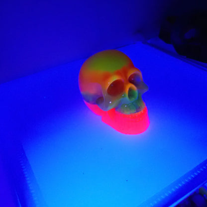 Angled view of the handmade resin Neon Skull under a UV light.  In this photo you can see the bands and swirls of yellow, orange, pink, blue, green, and brighter pink.