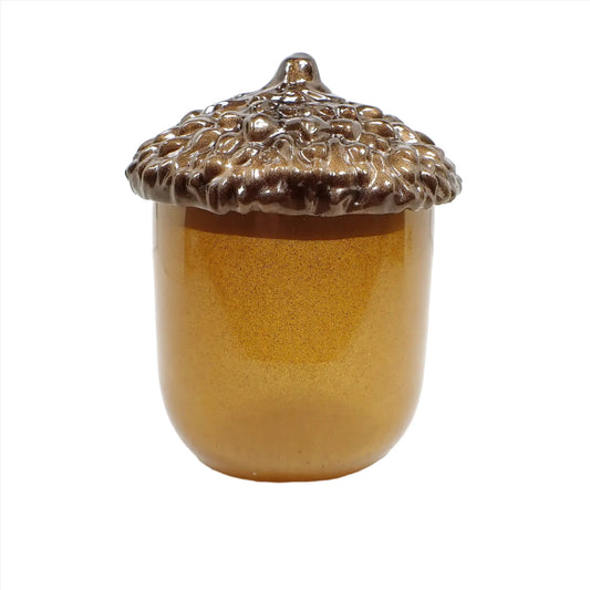 Side view of the handmade acorn resin trinket box jar. The lid is shaped like an acorn top and has pearly golden brown resin. The bottom part is tall with a rounded bottom and has a semi translucent golden honey yellow color resin.