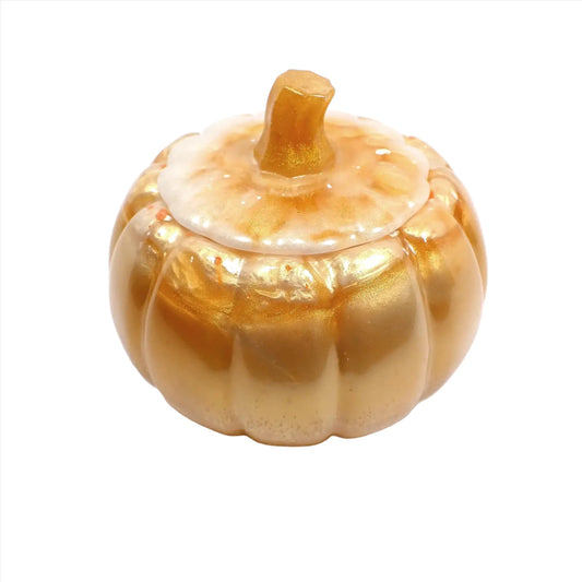 Angled view of the handmade resin pumpkin trinket dish jar. The bottom part is mostly peach in color with a metallic golden sheen. Around the top edge is some clear and golden pearly off white. The lid has pearly off white, peach, and metallic gold colors.