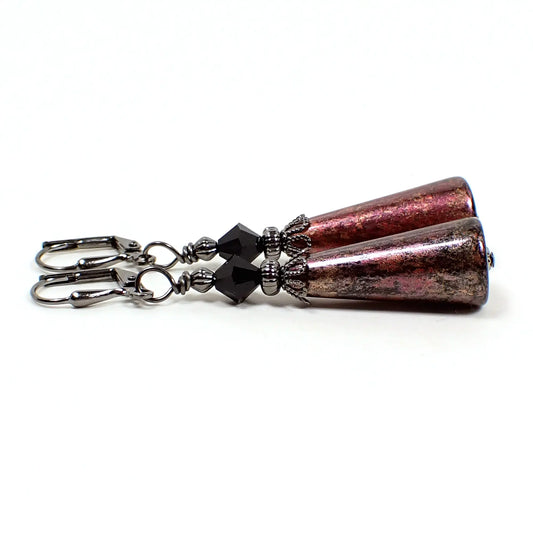 Side view of the handmade drop earrings with vintage acrylic beads. The top beads are faceted black bicone glass beads. The bottom beads are cone shaped acrylic and are black in color with metallic pink and gold colors brushed over the top. The metal is gunmetal gray in color.