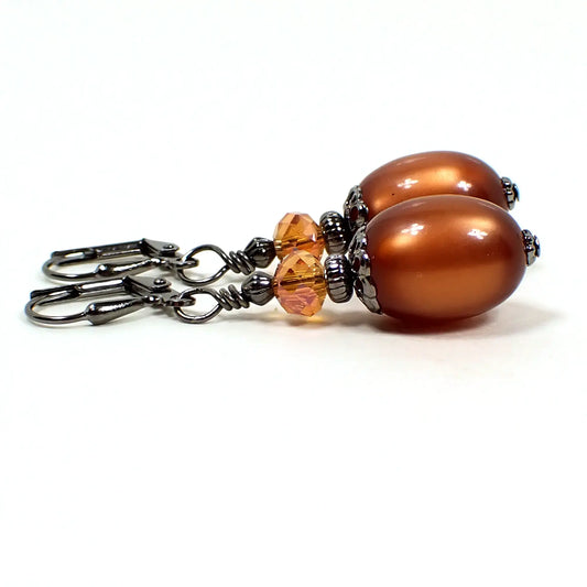Side view of the handmade drop earrings with vintage moonglow lucite beads. The metal is gunmetal gray in color. There are lucite oval beads at the bottom in a golden brown color. They have a glowy effect when the light hits them. The top beads are faceted glass and have shades of orange.