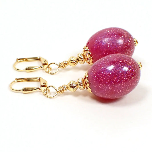 Side view of the handmade resin oval drop earrings. The metal is gold plated in color. The bottom resin beads are pink in color with tiny flecks of iridescent glitter.