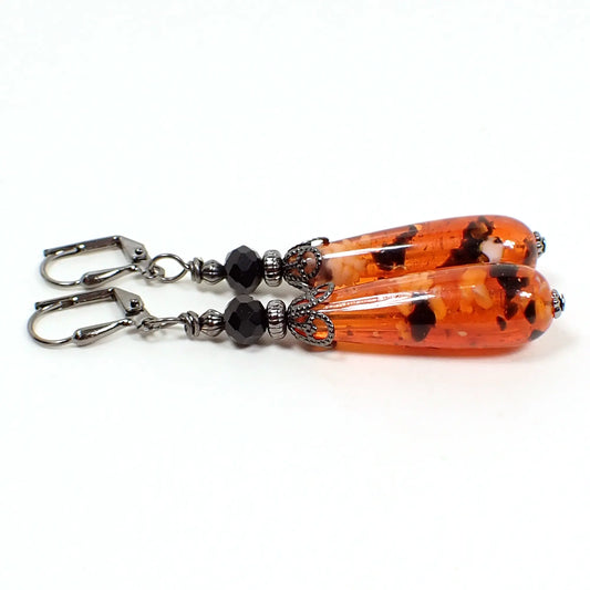Side view of the handmade Halloween earrings with vintage confetti lucite beads. The metal is gunmetal gray in color. The top beads are faceted black glass. The bottom lucite beads are teardrop shaped and are primarily orange in color with small chunks of white and black. Each beads is different from the other in pattern.